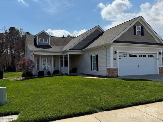 view of front of house with stone siding, concrete driveway, a front yard, roof with shingles, and a porch
