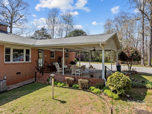 back of house featuring crawl space, a ceiling fan, brick siding, a lawn, and a shingled roof