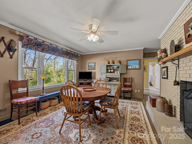 dining space featuring visible vents, crown molding, a brick fireplace, ceiling fan, and brick wall