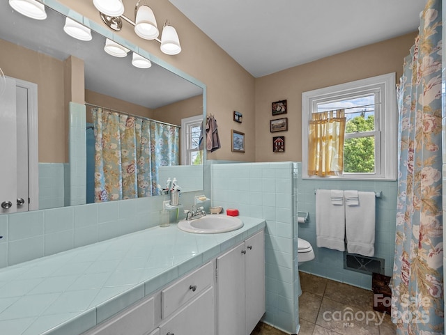 bathroom with tile walls, a wainscoted wall, toilet, tile patterned floors, and vanity