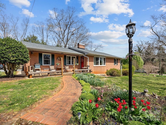 ranch-style house with a chimney, a front yard, covered porch, and brick siding