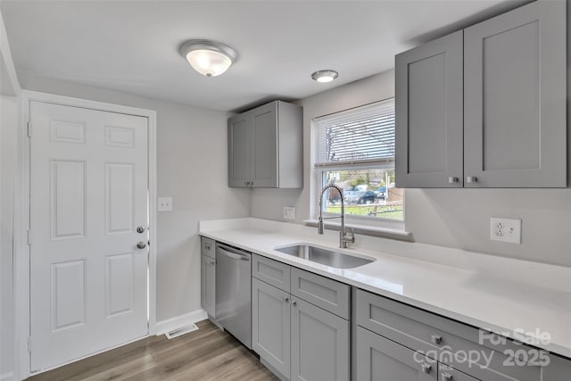 kitchen featuring dishwasher, a sink, light countertops, gray cabinetry, and light wood finished floors
