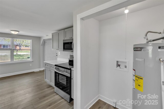 kitchen with gray cabinets, appliances with stainless steel finishes, wood finished floors, baseboards, and water heater