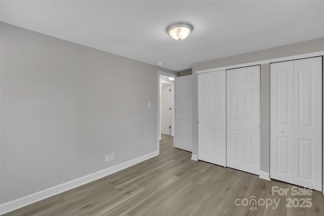unfurnished bedroom with baseboards, wood finished floors, and a closet