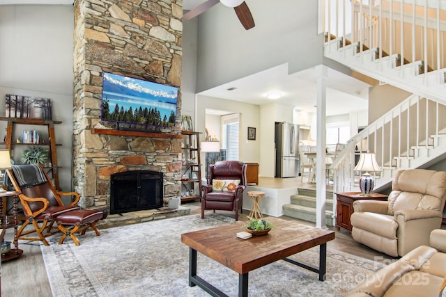 living area featuring stairway, a high ceiling, ceiling fan, a fireplace, and wood finished floors