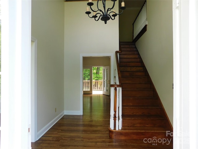 stairway with wood finished floors, a chandelier, baseboards, and a towering ceiling