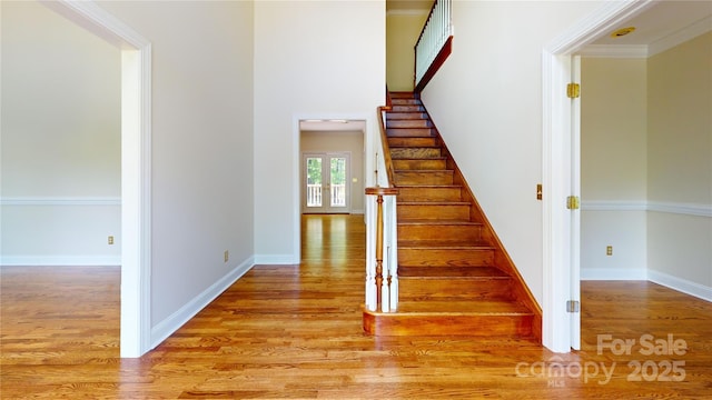 staircase featuring wood finished floors, baseboards, and crown molding
