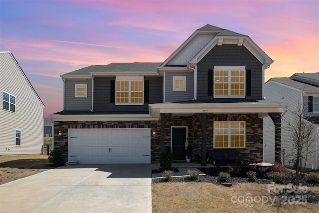 view of front of property with stone siding, an attached garage, board and batten siding, driveway, and covered porch