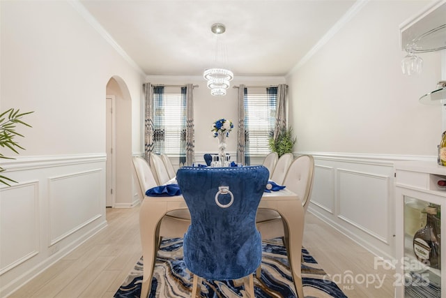 dining room featuring arched walkways, crown molding, light wood finished floors, and wainscoting