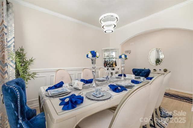 dining area with a wainscoted wall, crown molding, wood finished floors, a decorative wall, and arched walkways