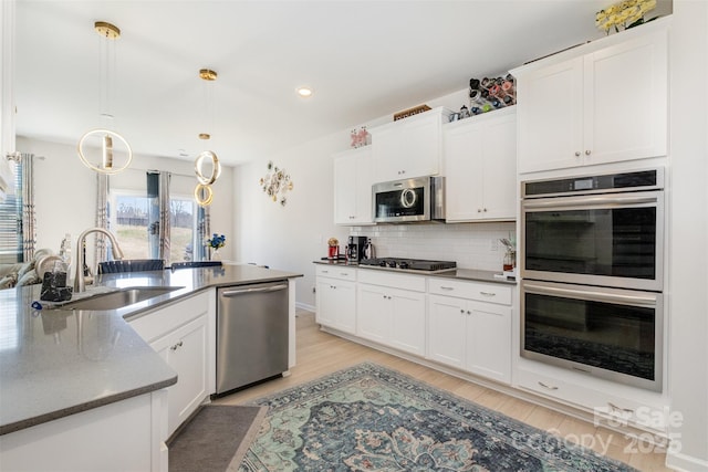 kitchen featuring decorative backsplash, white cabinets, appliances with stainless steel finishes, a sink, and light wood-type flooring