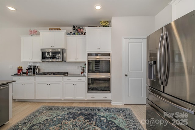 kitchen featuring white cabinetry, stainless steel appliances, decorative backsplash, dark countertops, and light wood-style flooring