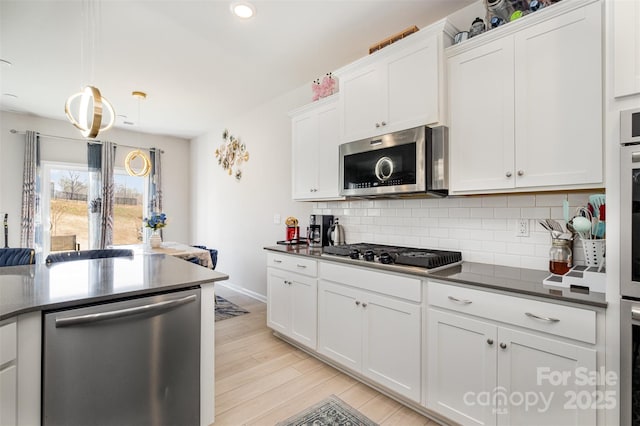 kitchen featuring white cabinets, light wood-style flooring, stainless steel appliances, dark countertops, and tasteful backsplash