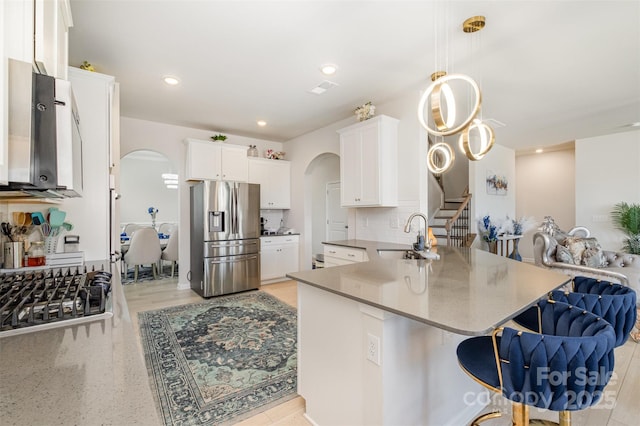 kitchen with open floor plan, stainless steel fridge, decorative backsplash, a sink, and arched walkways