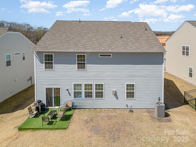 rear view of property with central AC, a yard, and a shingled roof