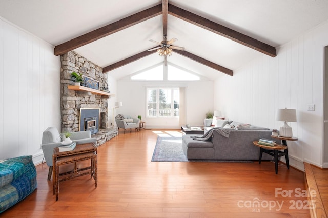 living area featuring ceiling fan, lofted ceiling with beams, a fireplace, and wood finished floors