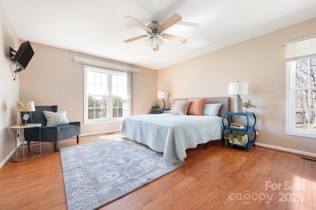 bedroom featuring baseboards, visible vents, wood finished floors, and multiple windows