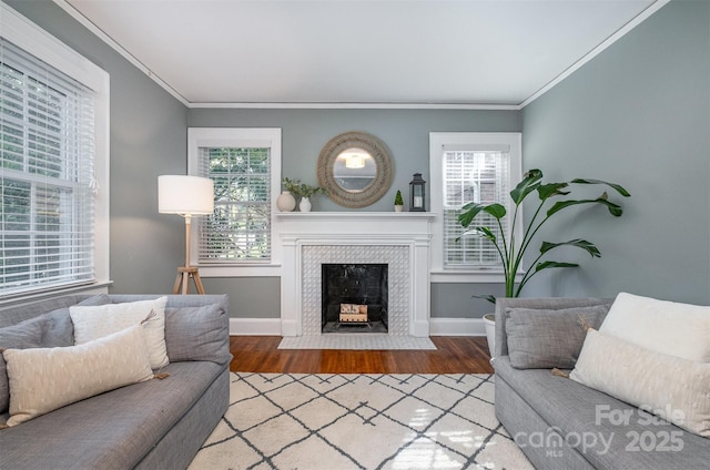 living area with baseboards, ornamental molding, wood finished floors, and a tiled fireplace