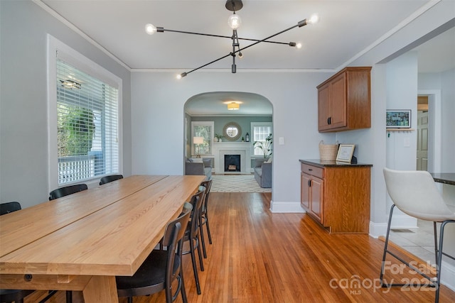 dining area featuring light wood-style flooring, arched walkways, crown molding, and a wealth of natural light