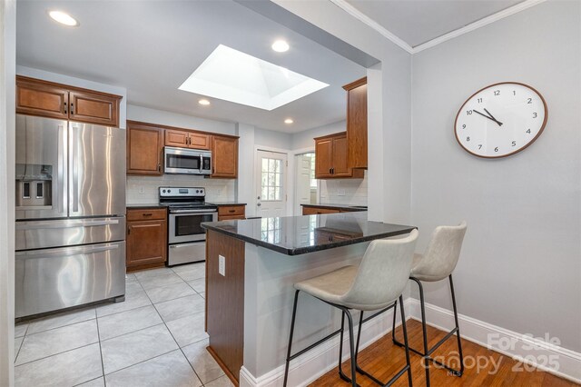 kitchen featuring a skylight, appliances with stainless steel finishes, tasteful backsplash, and a breakfast bar