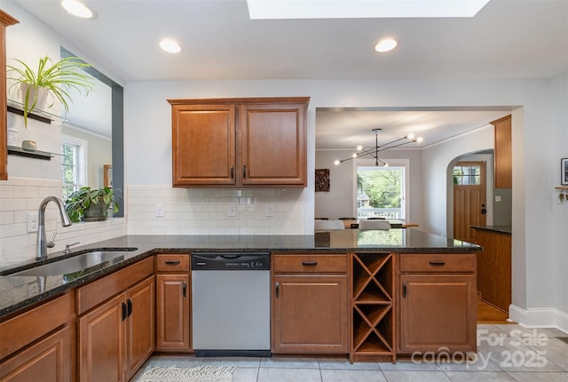 kitchen featuring a sink, a peninsula, stainless steel dishwasher, brown cabinets, and arched walkways