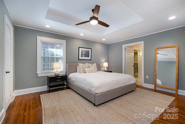 bedroom featuring a tray ceiling, recessed lighting, ornamental molding, baseboards, and wood finished floors