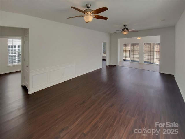 unfurnished room featuring baseboards, a ceiling fan, and dark wood finished floors