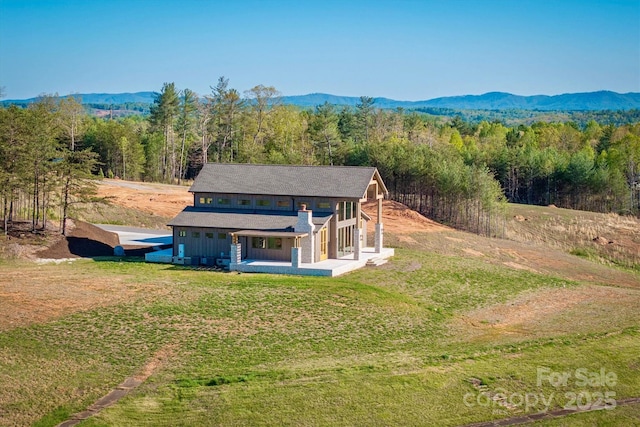 rear view of property featuring a mountain view, a porch, a forest view, and a lawn