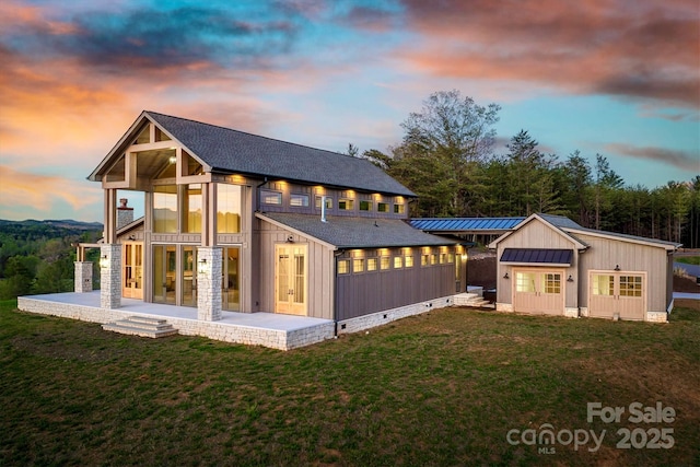 back of property at dusk with a lawn, a standing seam roof, board and batten siding, and french doors
