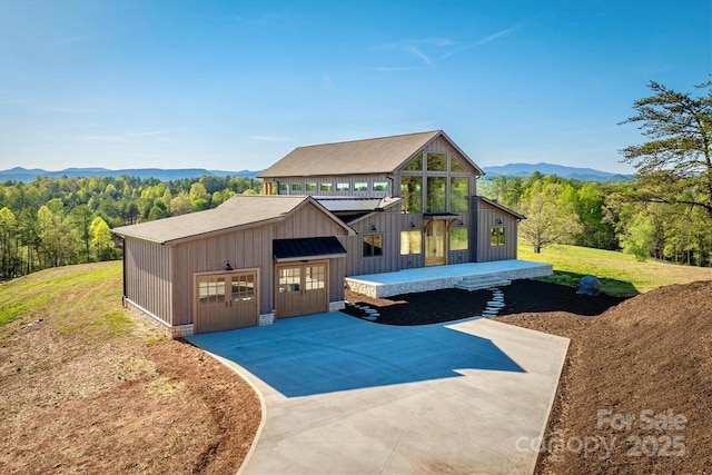 exterior space with a wooded view, board and batten siding, a mountain view, and a garage