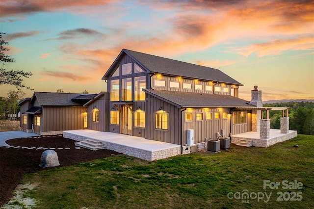 rear view of house featuring board and batten siding, a patio area, a yard, and central air condition unit