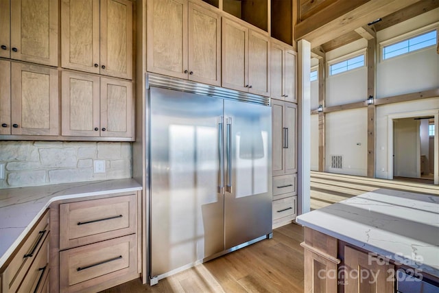 kitchen with built in refrigerator, light stone countertops, decorative backsplash, and light wood-type flooring