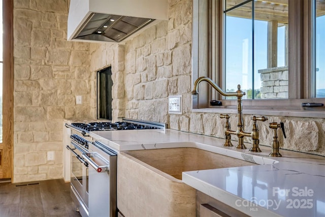 kitchen with a sink, a wealth of natural light, stainless steel range, and wall chimney exhaust hood