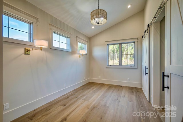 spare room featuring a chandelier, a barn door, light wood finished floors, baseboards, and lofted ceiling