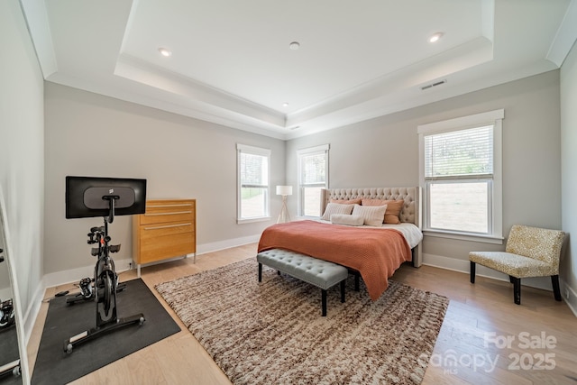 bedroom featuring baseboards, visible vents, wood finished floors, and a raised ceiling