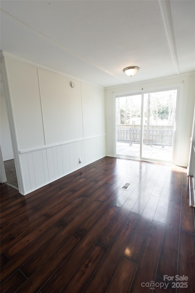 spare room featuring visible vents, a decorative wall, and dark wood-style flooring
