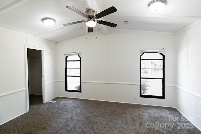 unfurnished room featuring ceiling fan, dark carpet, a decorative wall, and vaulted ceiling with beams