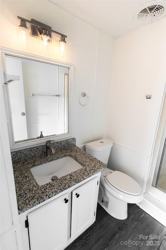bathroom featuring visible vents, walk in shower, toilet, wood finished floors, and vanity