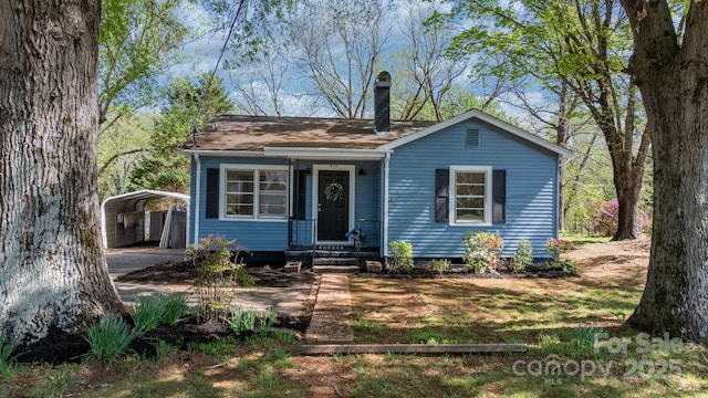 bungalow featuring a carport, concrete driveway, and a chimney