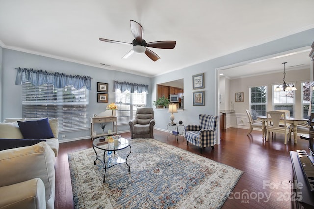 living room with crown molding, ceiling fan with notable chandelier, visible vents, wainscoting, and dark wood-style floors