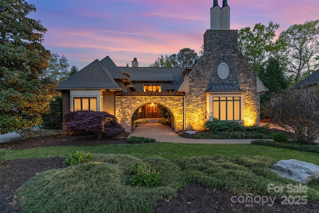 view of front of property featuring stone siding, a lawn, and a chimney