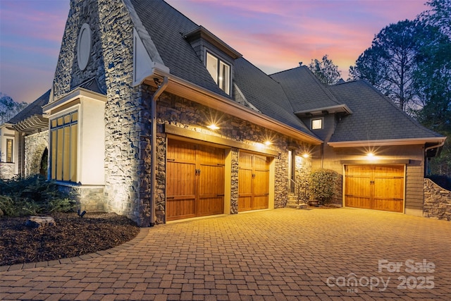 view of front of home with a garage, stone siding, and decorative driveway