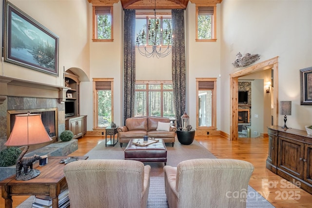 living area featuring light wood-style floors, a fireplace, arched walkways, a high ceiling, and baseboards
