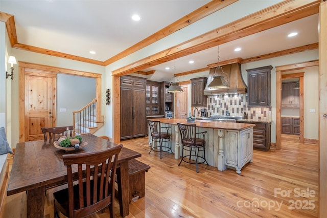 kitchen featuring custom exhaust hood, tasteful backsplash, light wood-type flooring, a kitchen breakfast bar, and a center island with sink
