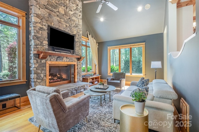 living room with a stone fireplace, a ceiling fan, plenty of natural light, and wood finished floors