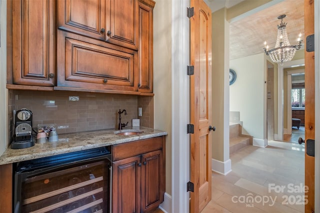 bar with a notable chandelier, baseboards, decorative backsplash, beverage cooler, and a sink
