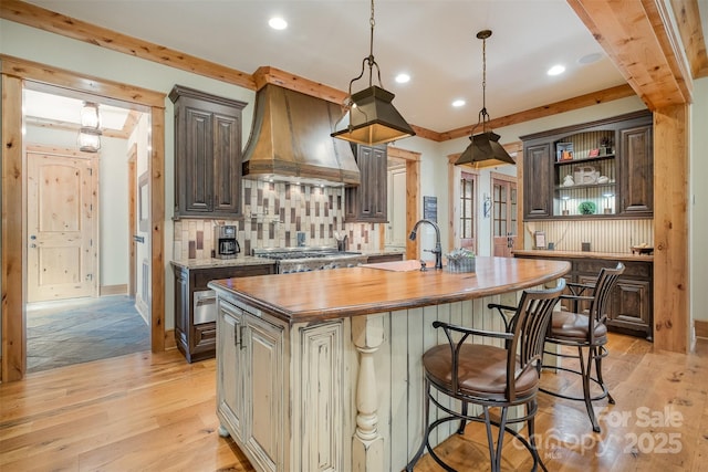 kitchen featuring custom exhaust hood, wood counters, tasteful backsplash, and light wood finished floors