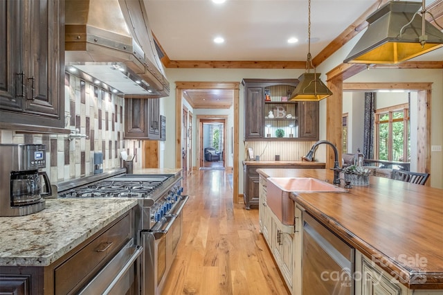 kitchen featuring butcher block countertops, light wood-style flooring, appliances with stainless steel finishes, range hood, and a sink
