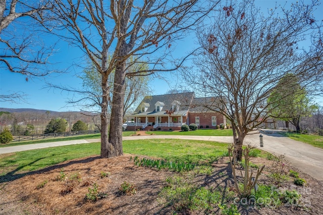cape cod-style house featuring covered porch, curved driveway, and a front lawn