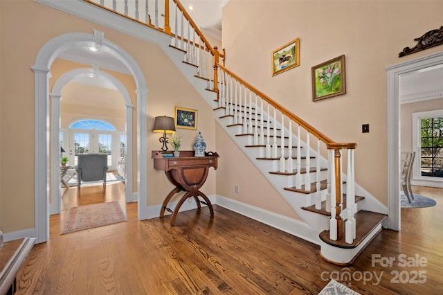 stairs with baseboards, ornate columns, a towering ceiling, wood finished floors, and arched walkways